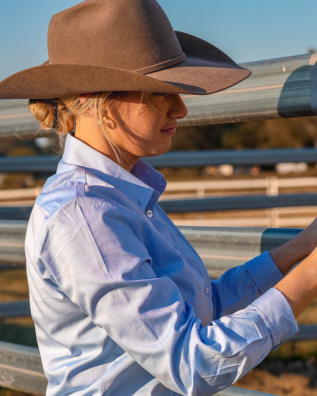 Person in cowboy hat and shirt unlocking a metal gate in an outdoor setting