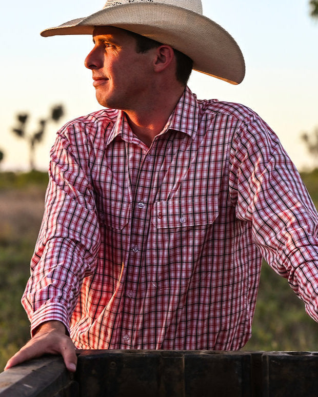 Man wearing a cowboy hat and plaid shirt standing in a field