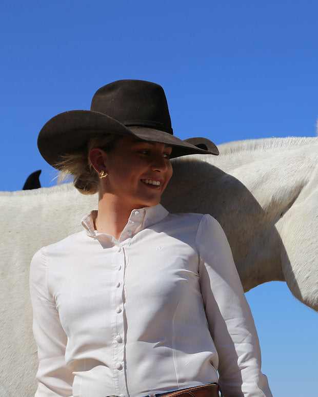 Woman in a cowboy hat standing next to a white horse against a clear blue sky