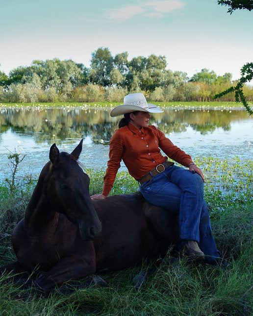 Person sitting on a horse by a lake with trees in the background
