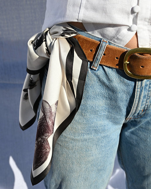Person wearing a patterned scarf around their neck with a white shirt and blue jeans.