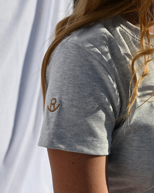 Person wearing a textured gray t-shirt with a small logo on the sleeve against a white background