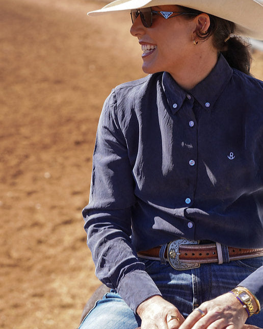 Person wearing a navy shirt and cowboy hat sitting on a horse in a dirt arena