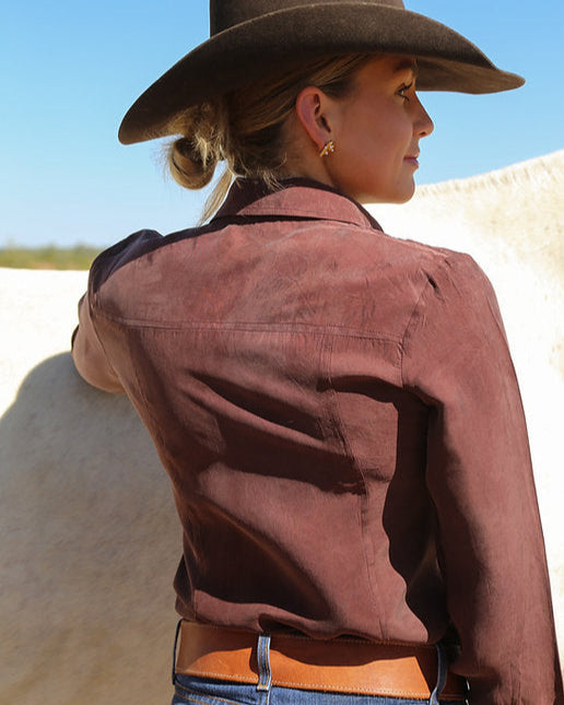 Person wearing a brown jacket and cowboy hat with a horse in the background
