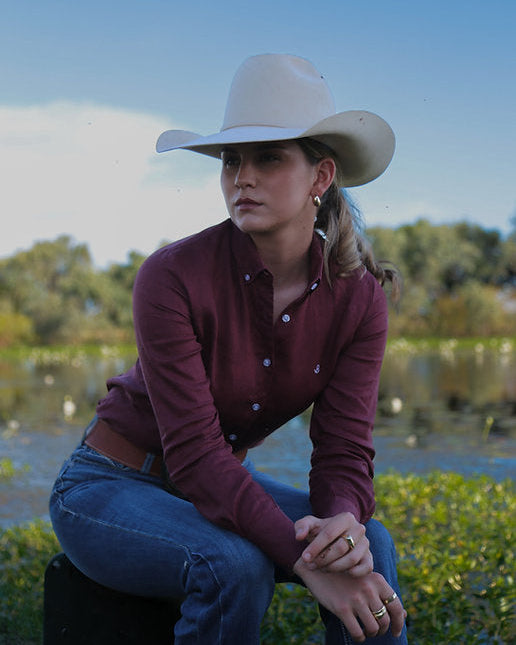 Woman wearing a cowboy hat sitting outdoors with a scenic background