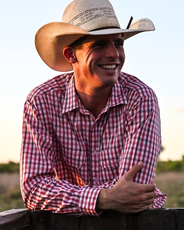 Man wearing a cowboy hat and checkered shirt in an outdoor setting