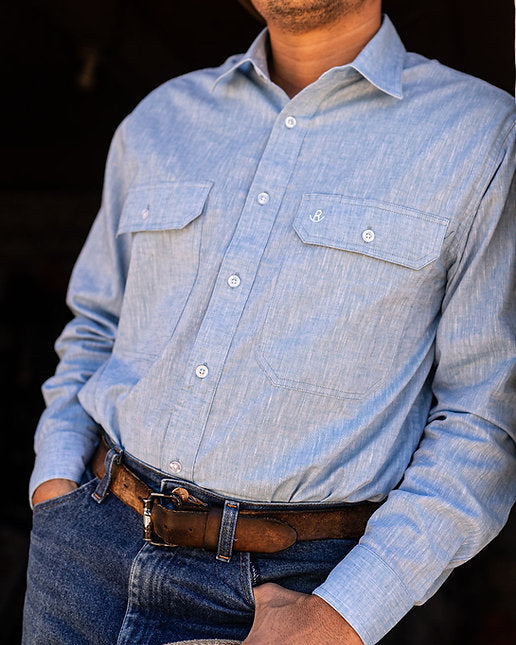 Person wearing a light blue denim shirt and dark jeans, holding a rope.