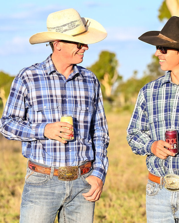 Two men in plaid shirts and cowboy hats standing in a field.