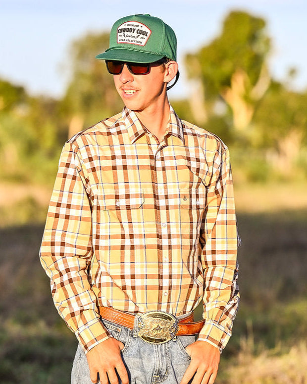 Man wearing a plaid shirt, jeans, and a green cap with a logo outdoors.