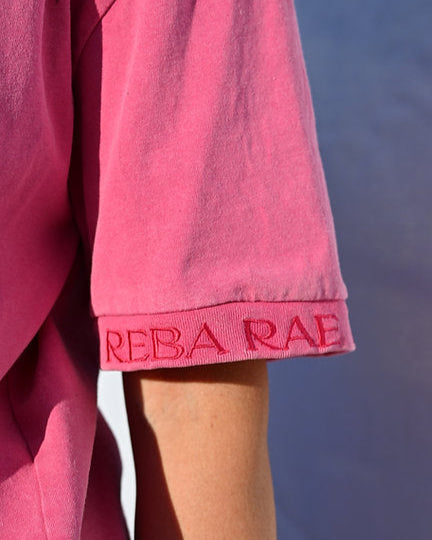 Close-up of a pink garment with 'REBA RAE' branding against a white background