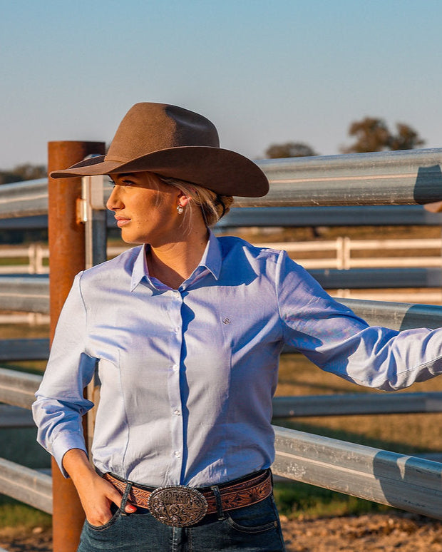 Two women wearing cowboy hats standing next to a metal fence with a clear sky background.